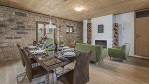 Ein Essbereich mit einem Holztisch, gedeckt für vier Personen, umgeben von grünen, gepolsterten Stühlen. Im Hintergrund sind eine Steinwand und eine Holzbalkendecke zu sehen.