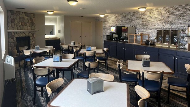 A restaurant with tables and chairs, a stone fireplace, and a kitchen area with appliances. - AmericInn by Wyndham Viroqua (Viroqua)