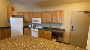 A kitchen with wooden cabinets, a white refrigerator, a microwave, a stove, and granite countertops. - AmericInn by Wyndham Viroqua (Viroqua)