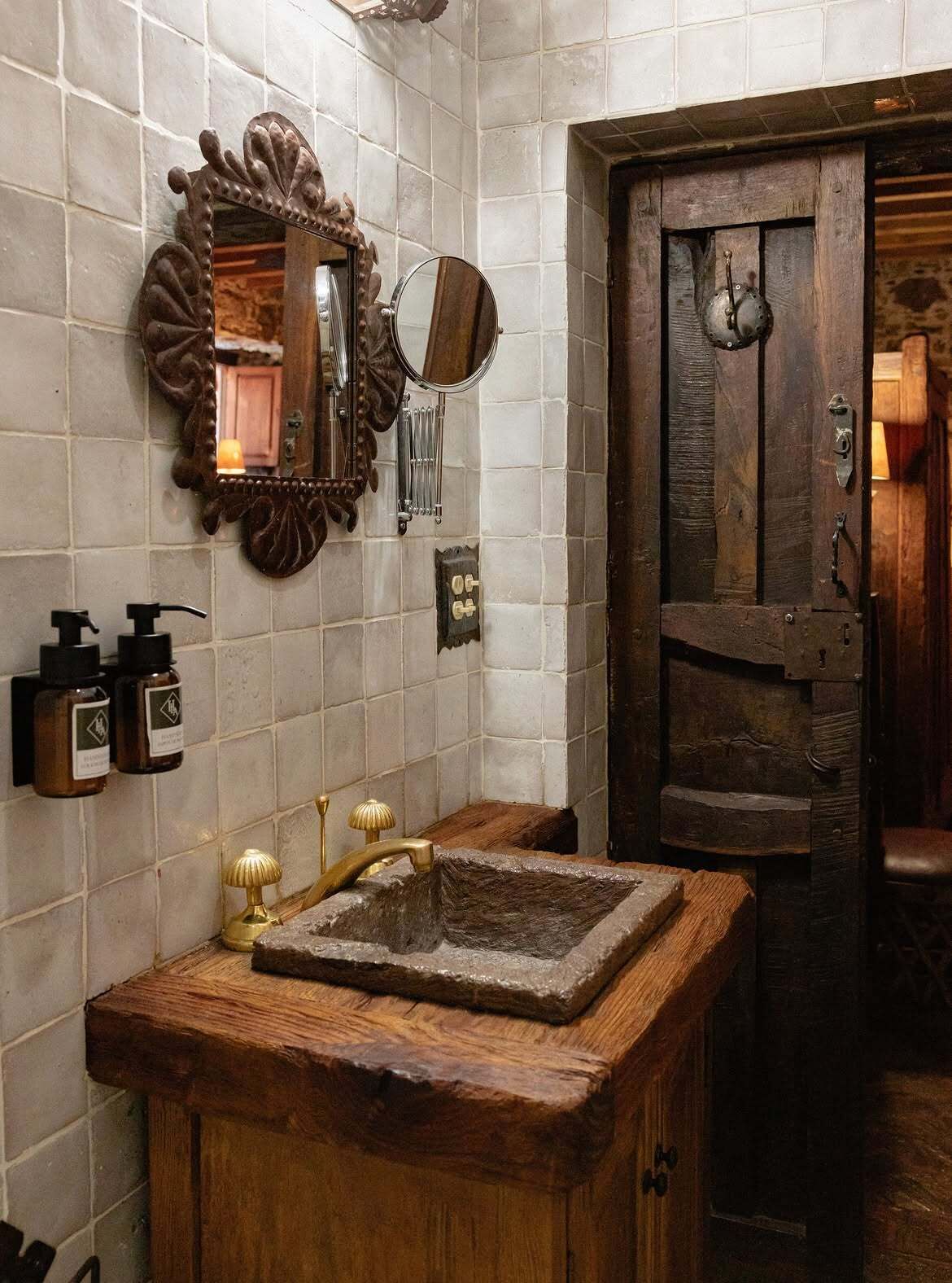 Un baño rústico con un lavamanos de madera, un espejo y una puerta.