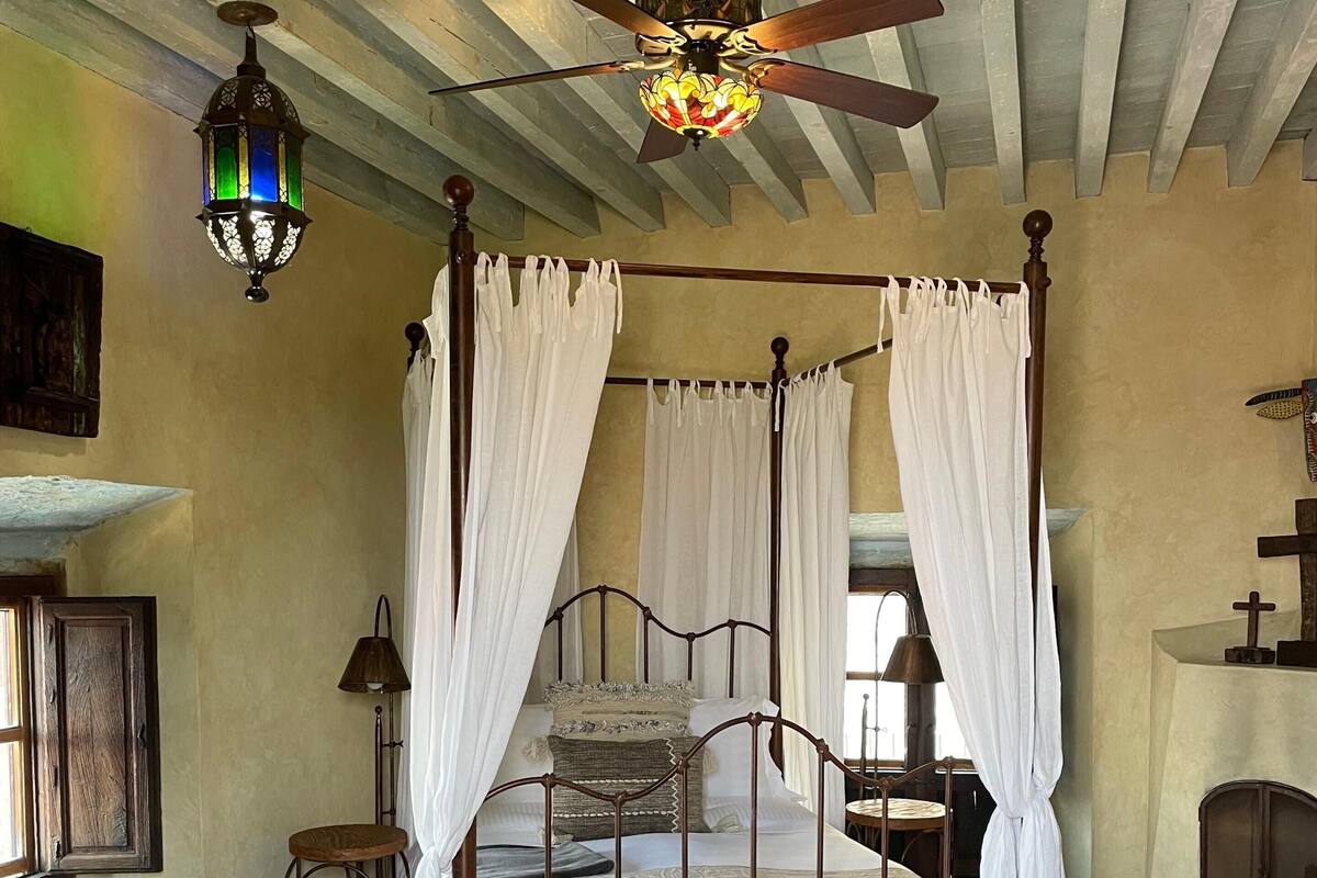 A four-poster canopy bed with a wooden bench, a patterned rug, and a ceiling fan.