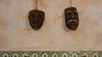 A bathroom with four wooden masks hanging on the wall, a tiled floor with a green and beige pattern, and two white towels on a rack.