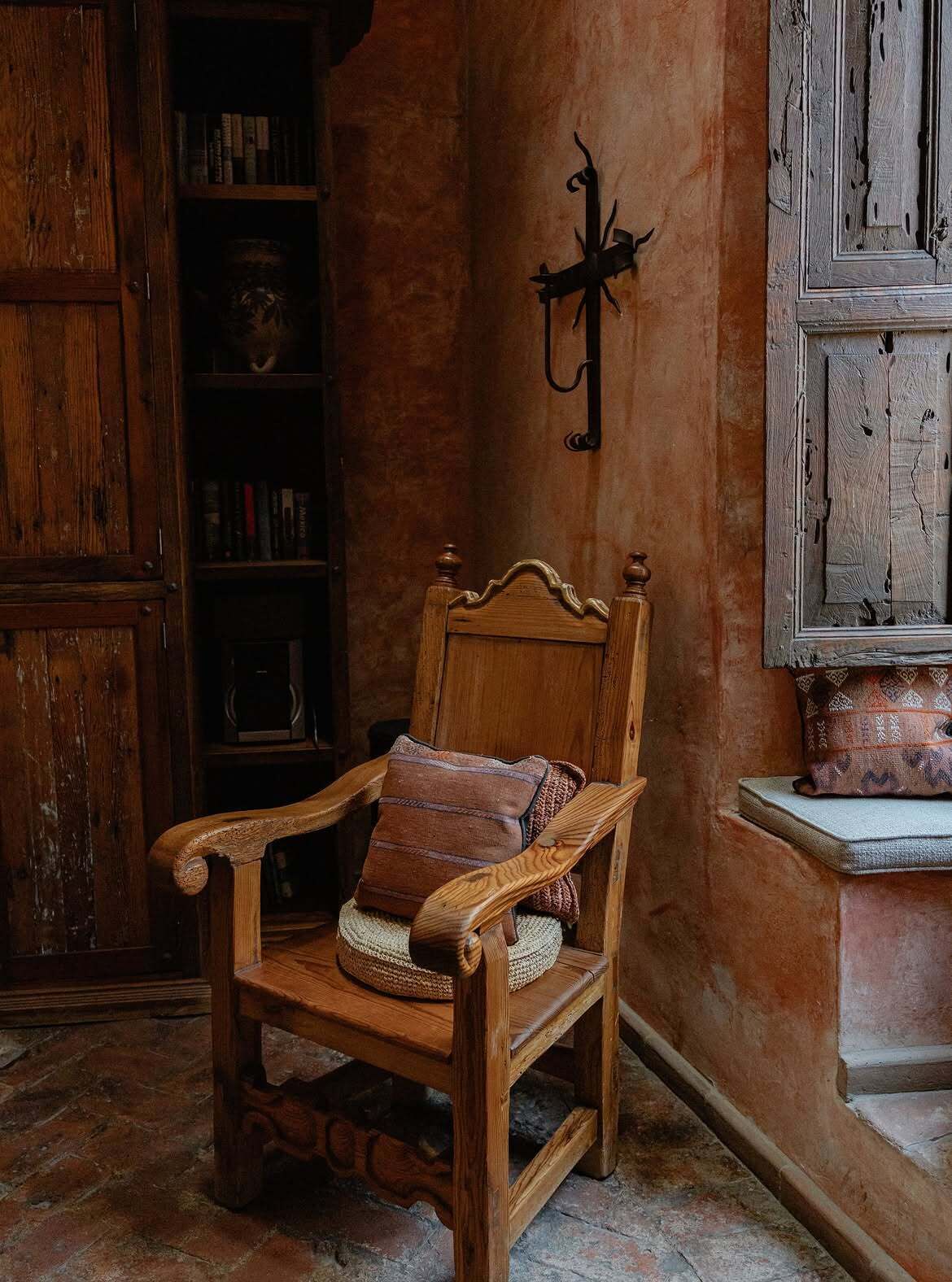A wooden chair with a cushion, a bookshelf, and a wall-mounted coat rack in a room with a rustic aesthetic.