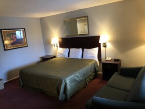 A hotel room with a large bed, two bedside tables with lamps, a chair, a framed picture on the wall, and a mirror above the bed. - Latham Inn (Latham)