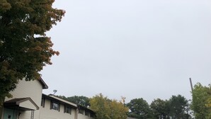 A two-story building with a gated entrance, a parking lot, and a street view with parked cars and trees. - Latham Inn (Latham)