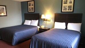 A hotel room with two beds, a nightstand, a lamp, and framed pictures on the wall. - Latham Inn (Latham)