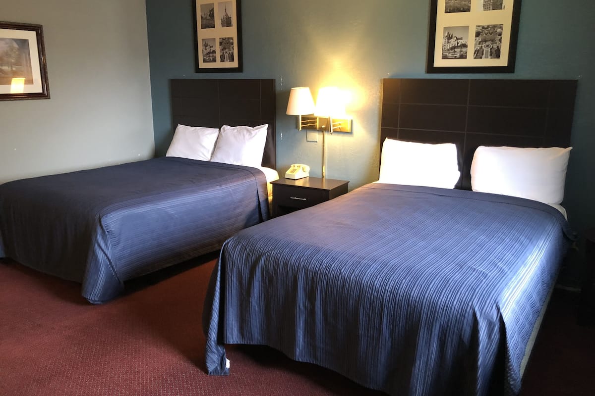 Quarto de hotel com duas camas, uma mesinha de cabeceira, abajur e quadros nas paredes.