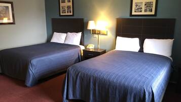 A hotel room with two beds, a nightstand, a lamp, and framed pictures on the wall.
