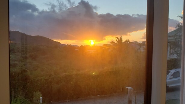 A sunset view through a window, with a road and vegetation in the foreground.
