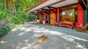 A rustic cabin with a red exterior, large windows, and a covered porch area with hammocks. - Hotel Casa Vito (Cahuita)