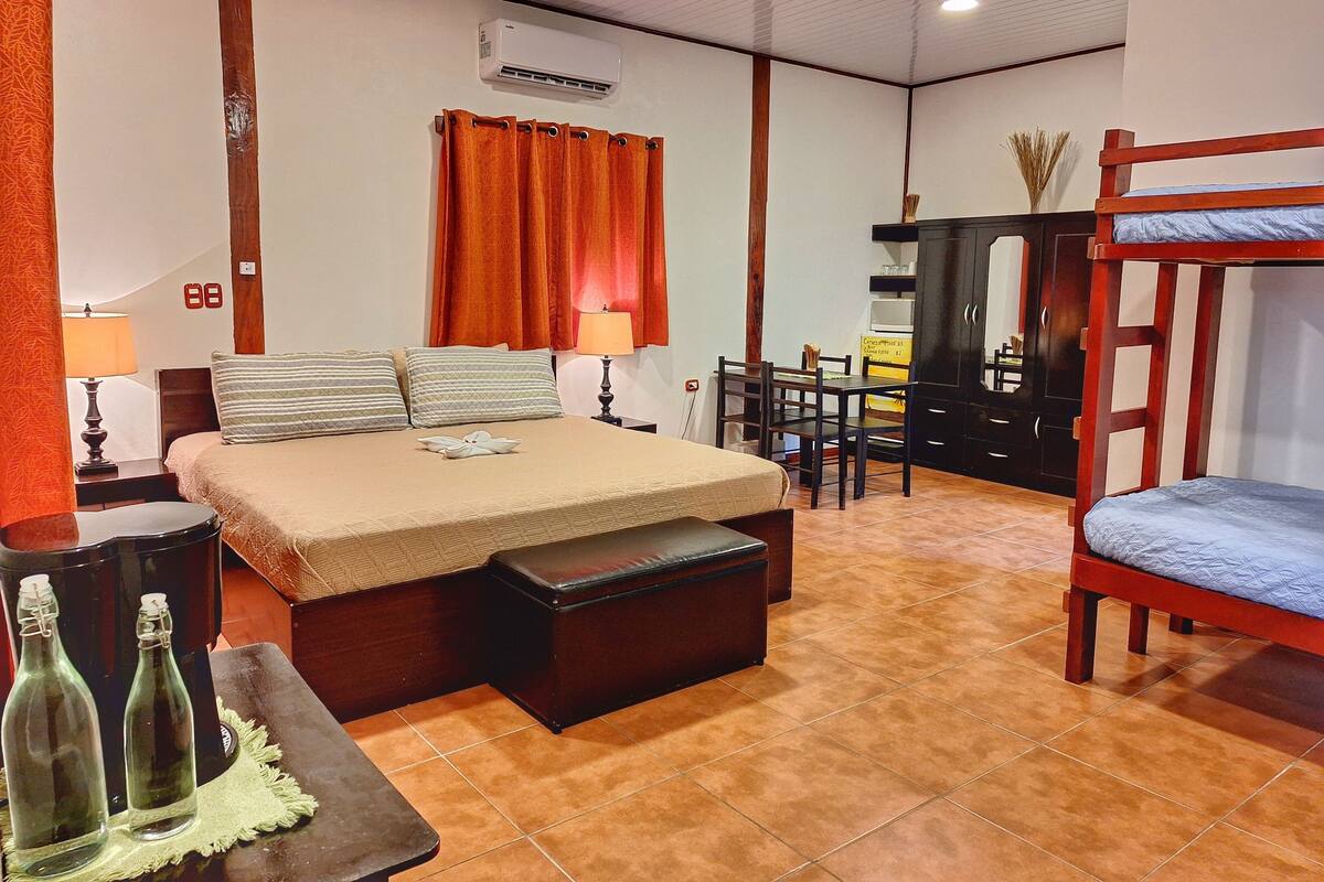 A bedroom with a bed, bedside tables, a desk, a bunk bed, and an air conditioning unit.