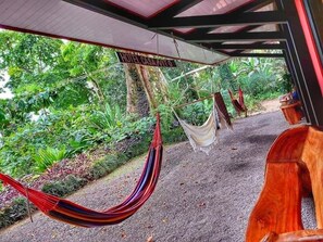 A hammock under a sign that reads "HOTEL CASA NADA" with a view of lush greenery and a wooden bench. - Hotel Casa Vito (Cahuita)