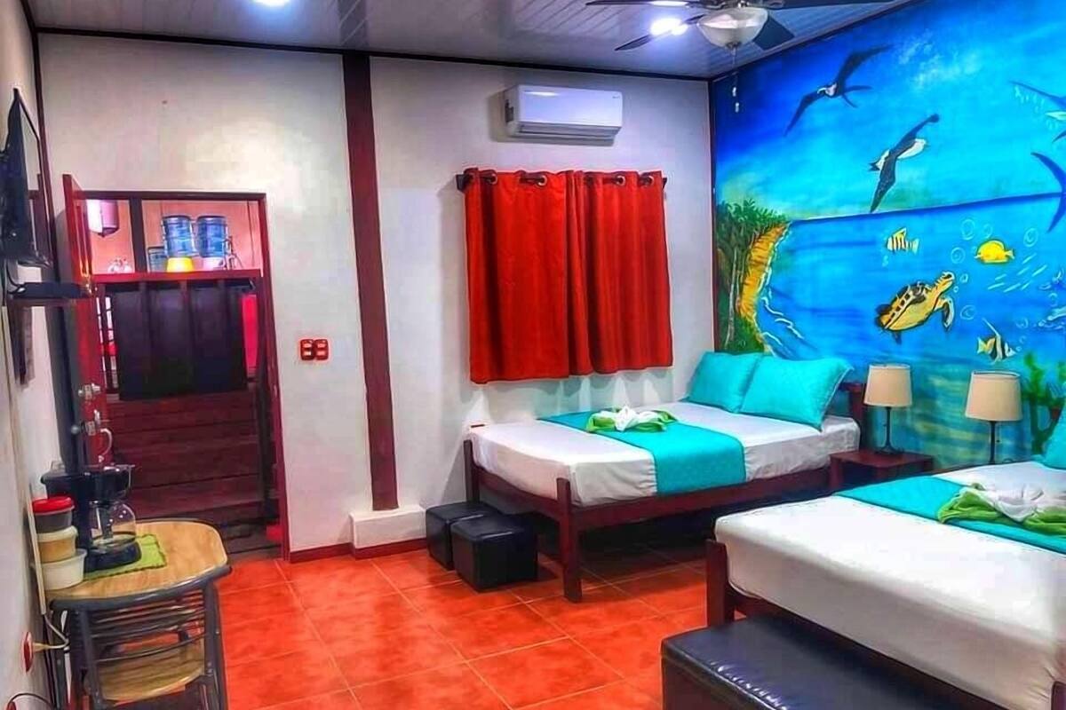 A hotel room with two beds, a red curtain, a ceiling fan, and an underwater mural on the wall.