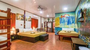 A hotel room with a large bed, a smaller bed, a desk, and a chair. There is a painting on the wall and a ceiling fan. - Hotel Casa Vito (Cahuita)