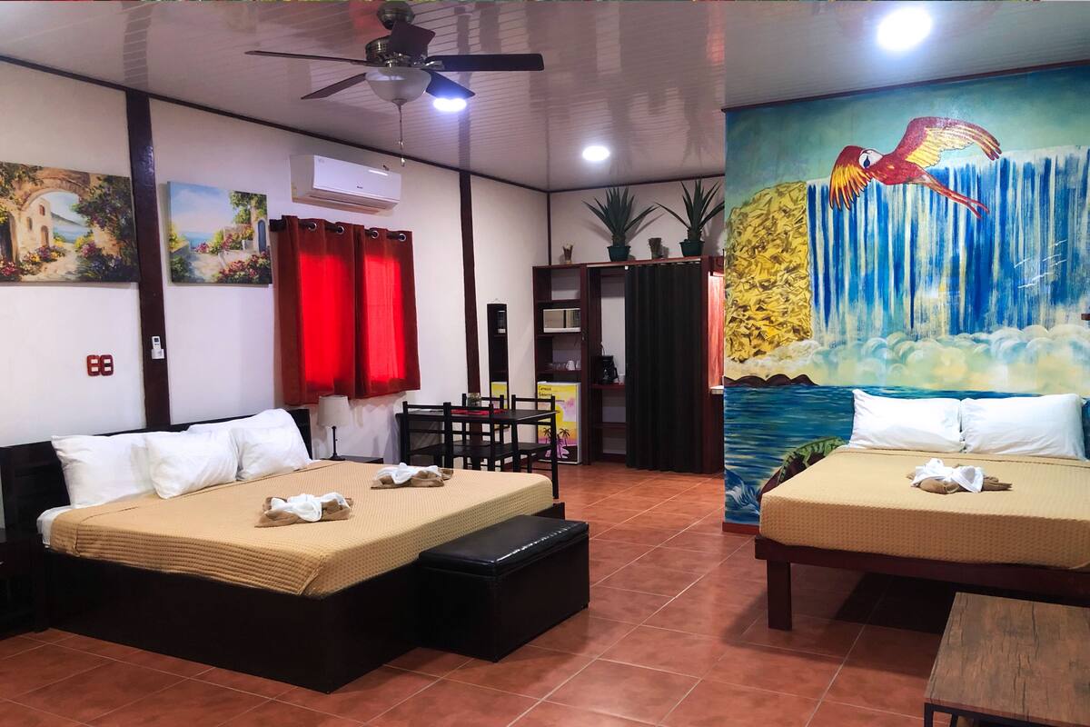 A hotel room with two beds, a ceiling fan, a painting of a bird, and a mural of a waterfall.