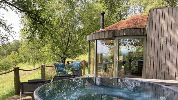 A hot tub on a wooden deck with a glass enclosure and a view of a garden. - Luxury and Peaceful 1-bed Roundhouse With Hot Tub (Glasgow)