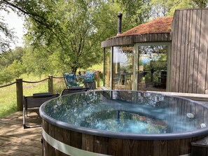 A hot tub on a wooden deck with a glass enclosure and a view of a garden. - Luxury and Peaceful 1-bed Roundhouse With Hot Tub (Glasgow)