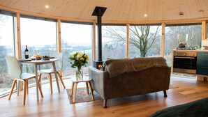 A cozy living room with a fireplace, a dining area with a table and chairs, and a view of the outdoors. - Luxury and Peaceful 1-bed Roundhouse With Hot Tub (Glasgow)