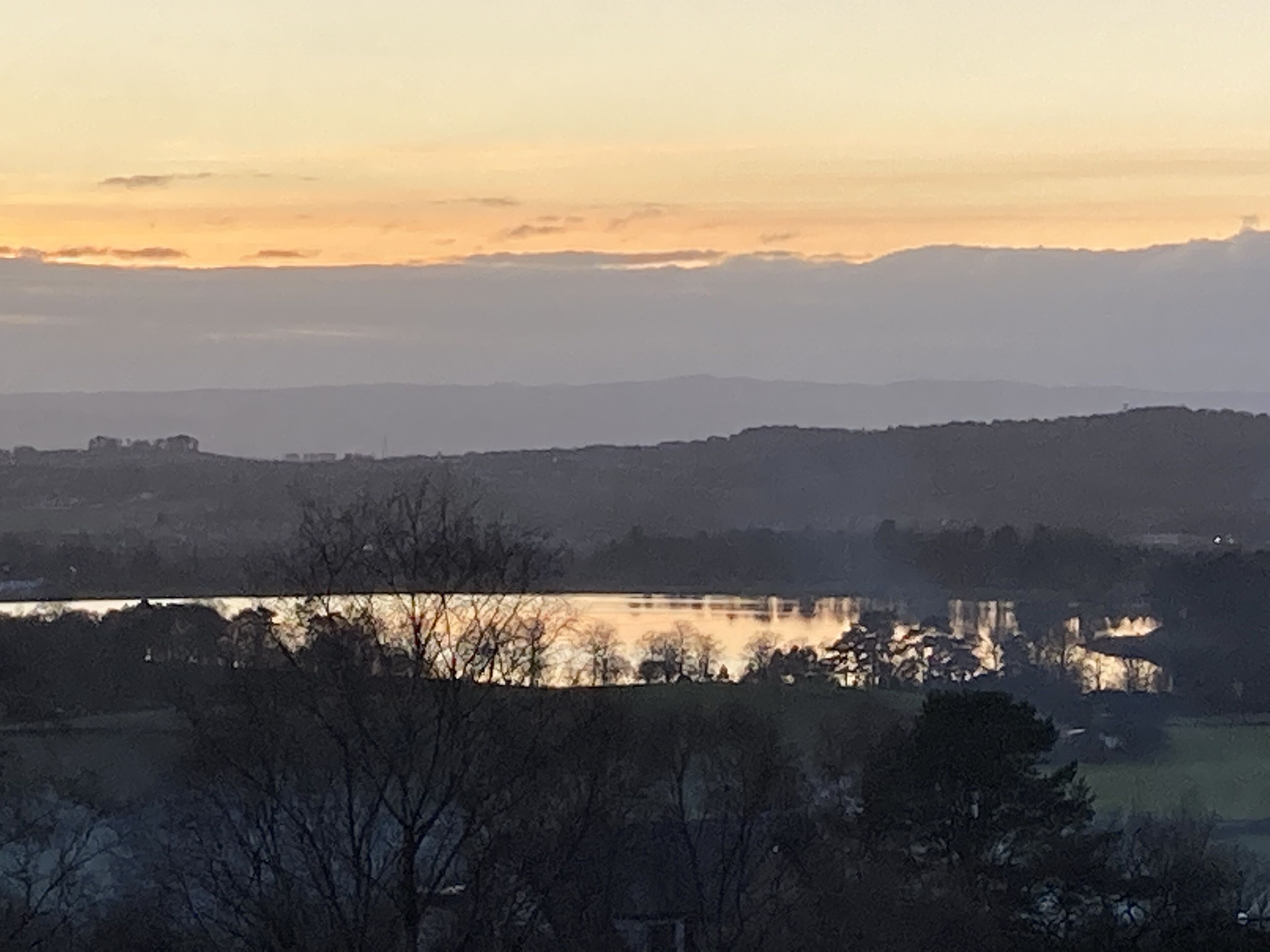 A landscape with a body of water reflecting the sky, surrounded by hills and trees.