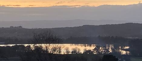 A landscape with a body of water reflecting the sky, surrounded by hills and trees.