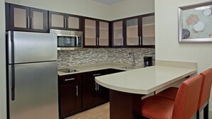 A modern kitchen with dark cabinets, stainless steel appliances, a tiled backsplash, and a bar area with red cushioned chairs.