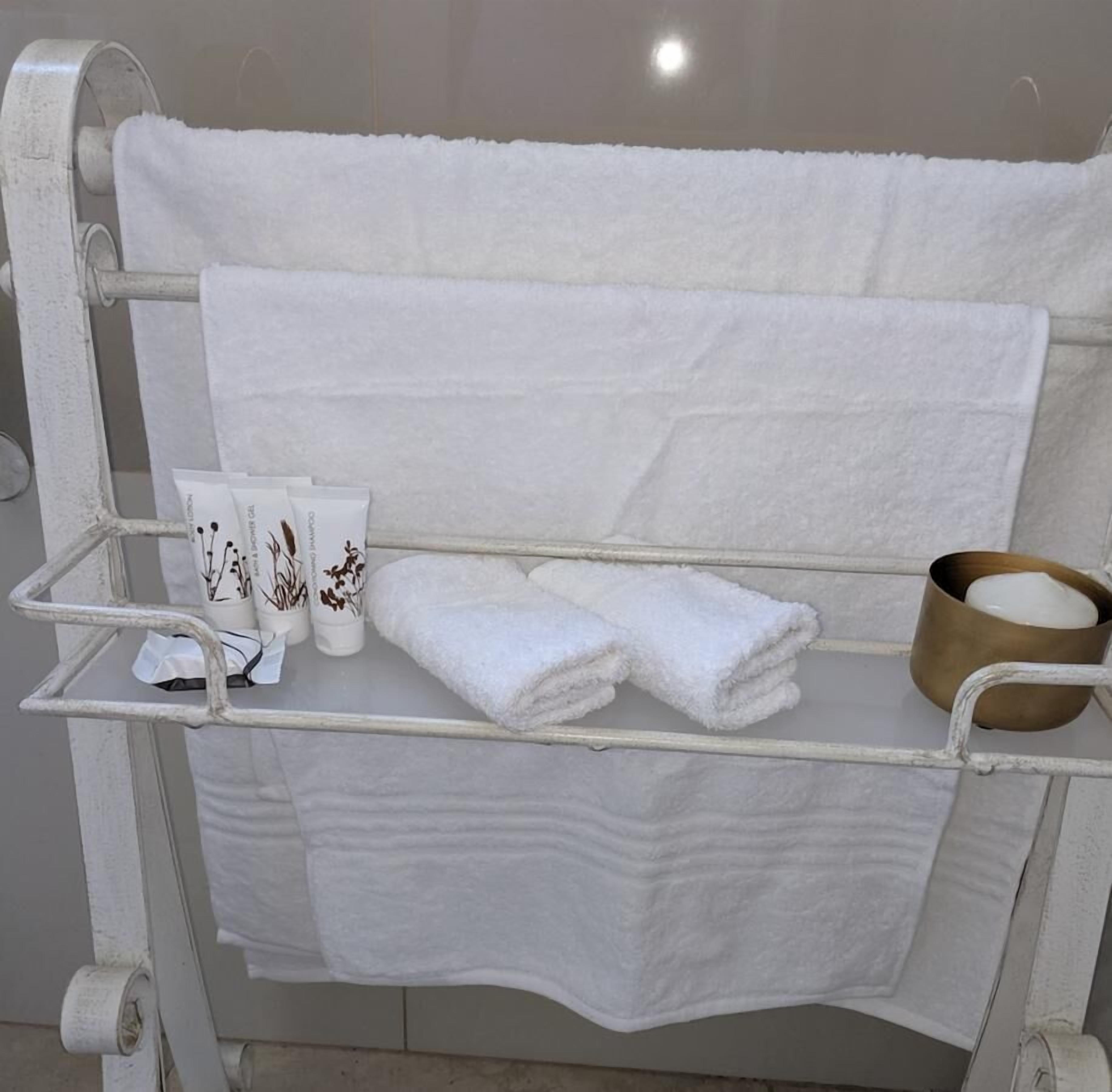 A metal towel rack with folded towels, a small container, and a tube of cream.