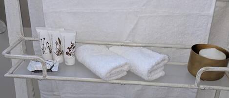 A metal towel rack with folded towels, a small container, and a tube of cream.