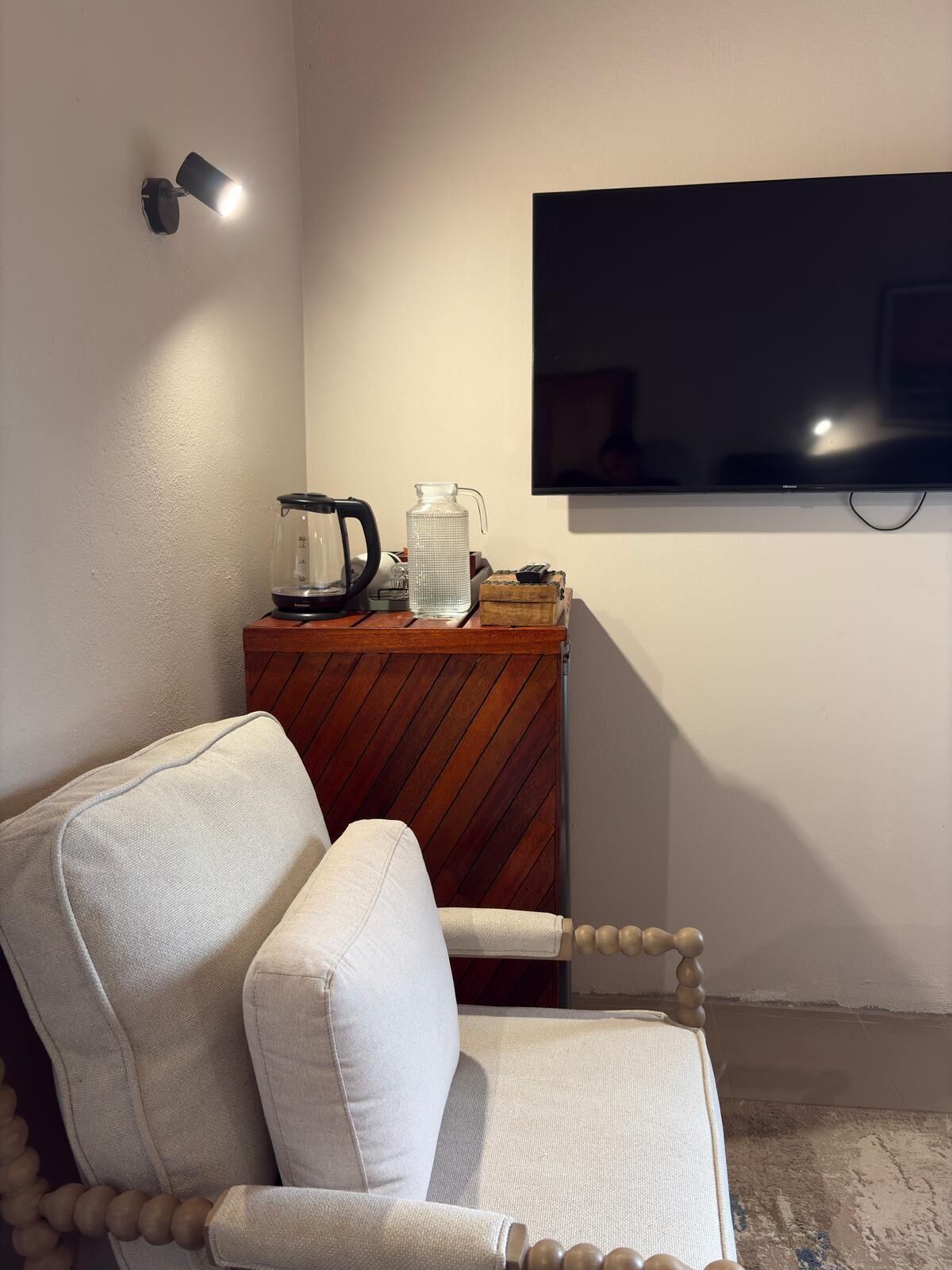 A room with a wooden cabinet, a television mounted on the wall, and a white chair with wooden accents.