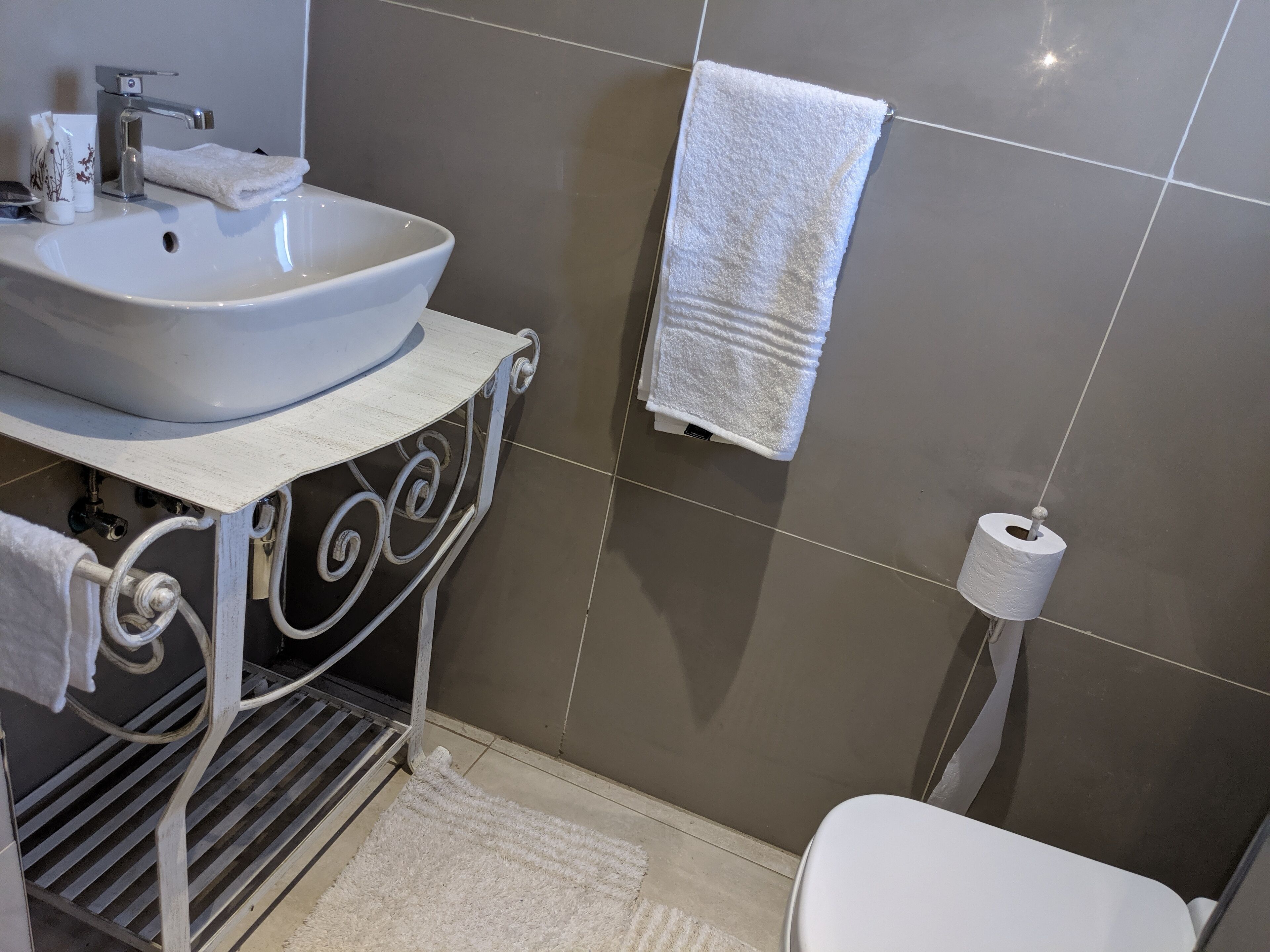 A bathroom with a white sink, a towel, a toilet, and a toilet paper holder.