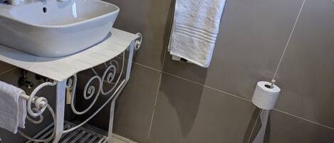 A bathroom with a white sink, a towel, a toilet, and a toilet paper holder.