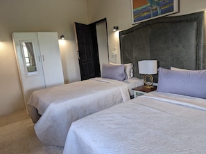 A hotel room with two beds, a wardrobe, a nightstand with a lamp, and a painting on the wall. - Sunbirds Lodge Chobe (Kasane)