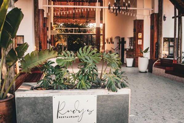 A restaurant entrance with a sign, potted plants, and a wooden bench.