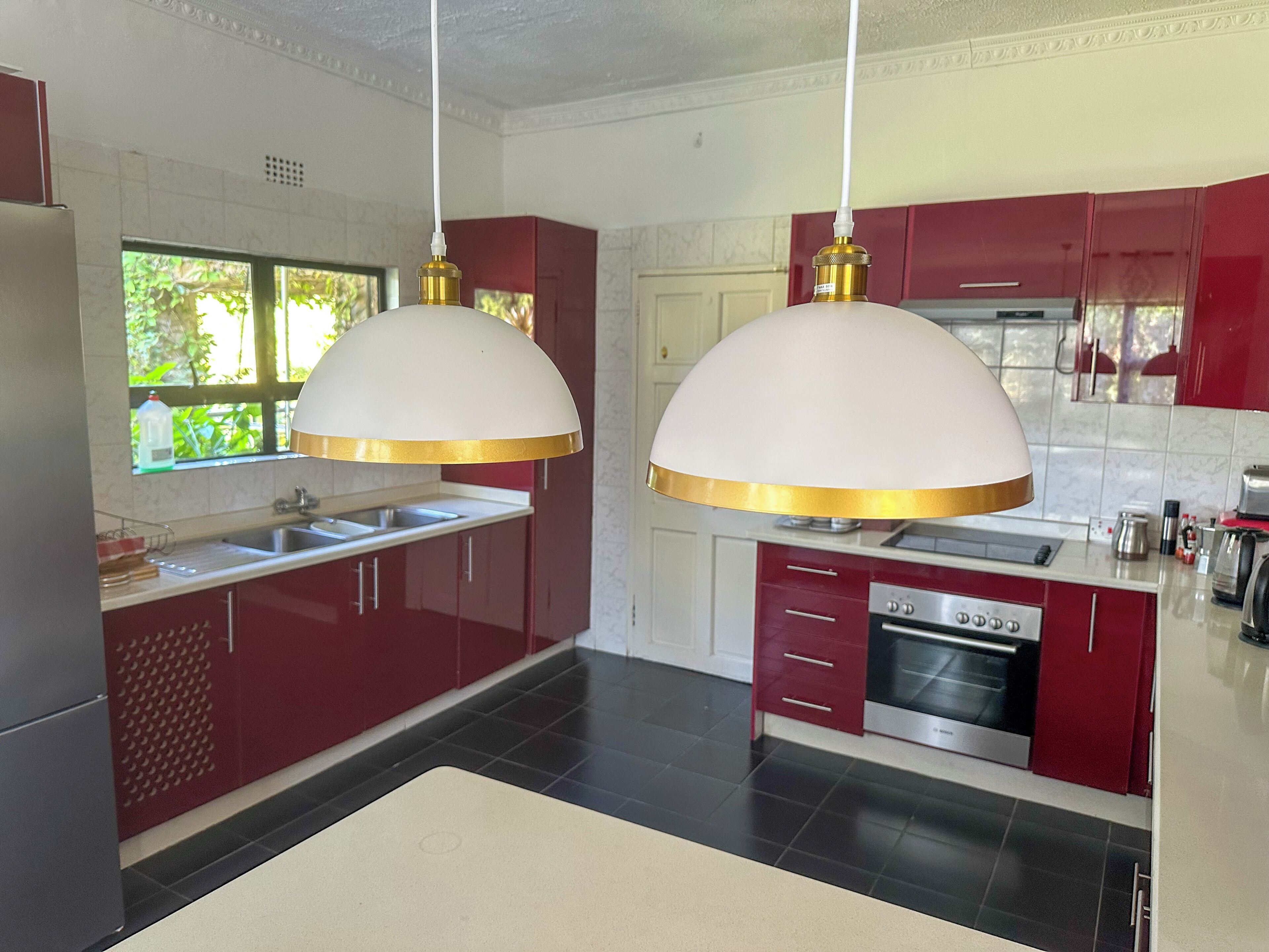 Una cocina moderna con dos lámparas colgantes, un horno empotrado y un ventanal con vistas al verdor.