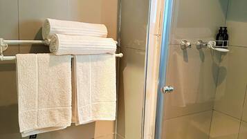 Un baño con cabina de ducha de vidrio, un perchero con toallas dobladas, un lavabo y un estante pequeño con artículos de aseo.