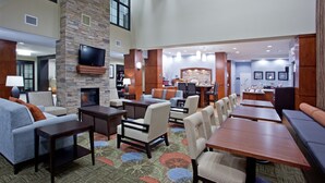 A spacious lobby with a fireplace, comfortable seating, and a television mounted on a stone wall. - Free Breakfast + Outdoor Pool + 24 Hour Fitness Center (Stafford)