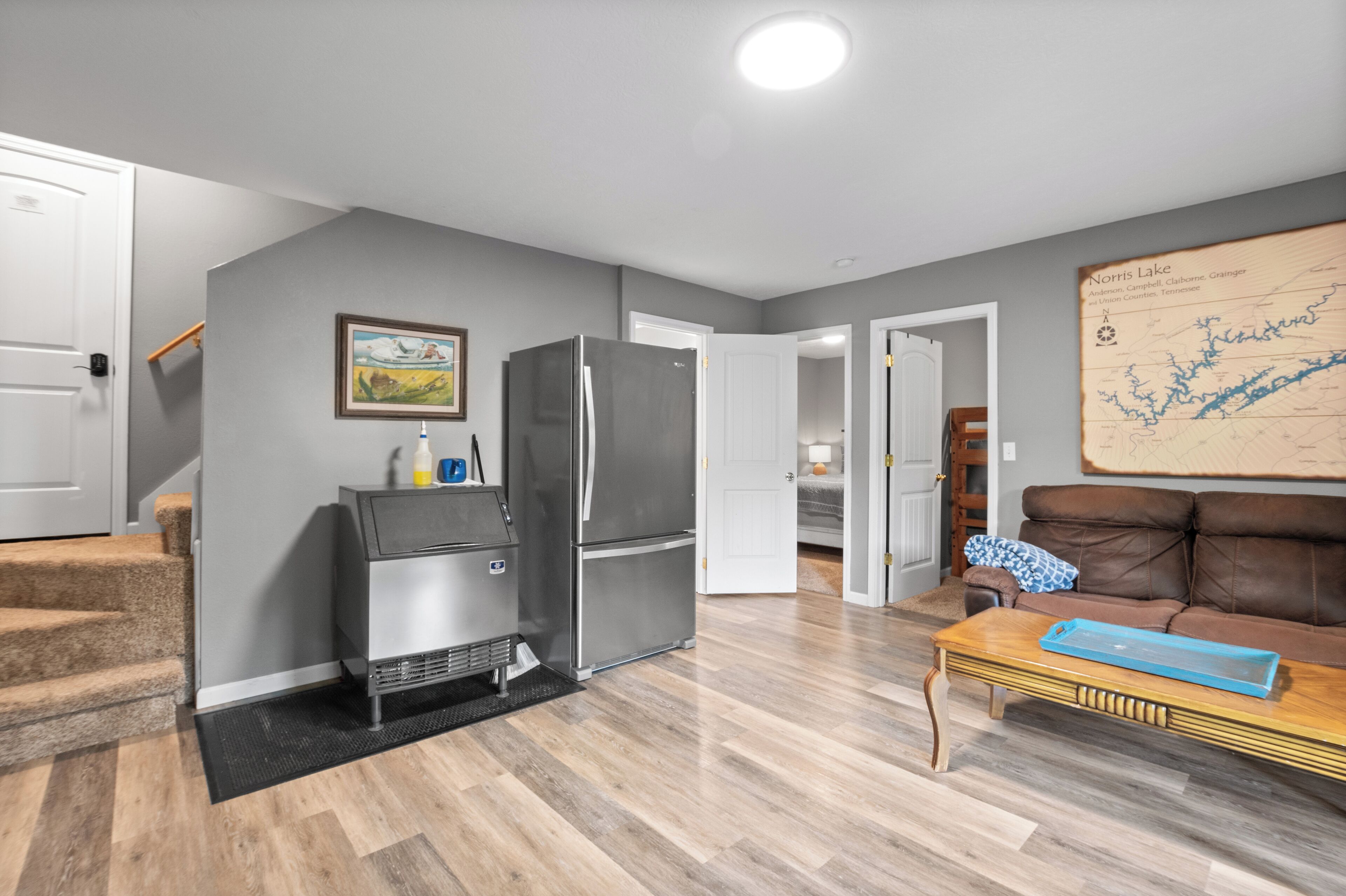 Una sala de estar moderna con una pared gris, piso de madera, un sofá de cuero marrón, una mesa de centro de madera, un refrigerador de acero inoxidable y un mapa en la pared.