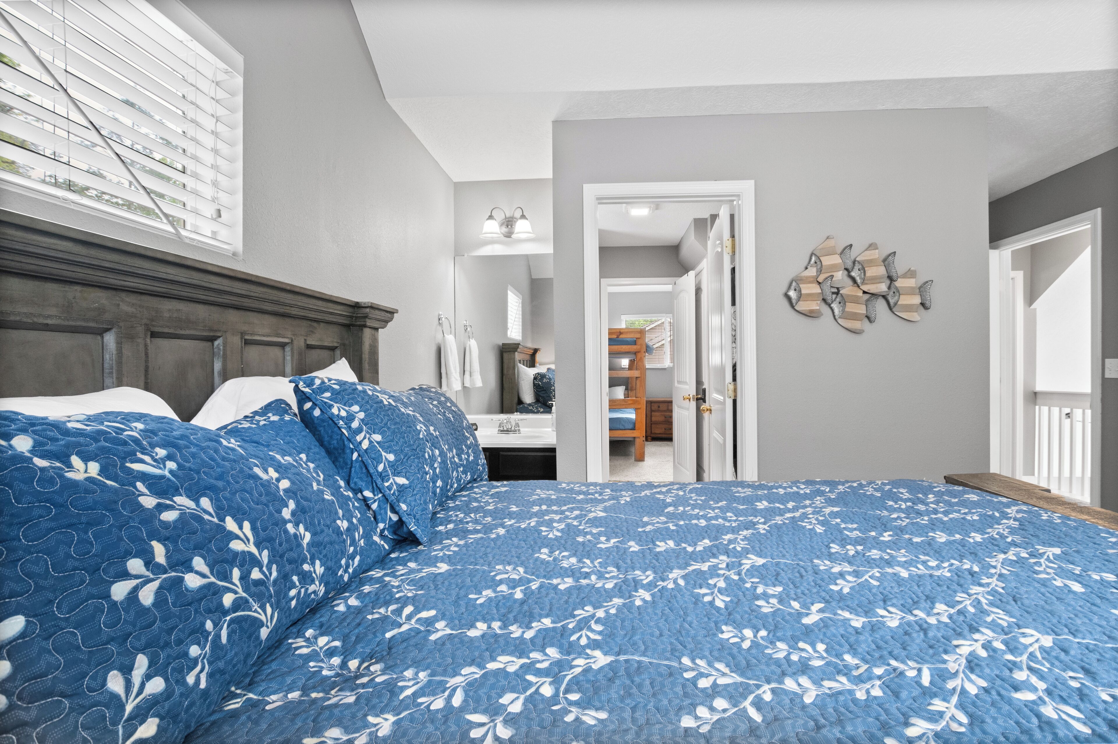 Une chambre avec un grand lit, une tête de lit en bois, une salle de bain avec un miroir et un porte-serviettes, et un couloir menant à un placard.