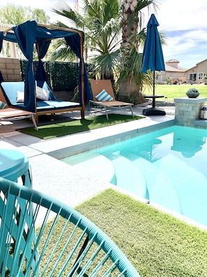 A pool area with lounge chairs, a pergola, and a palm tree.