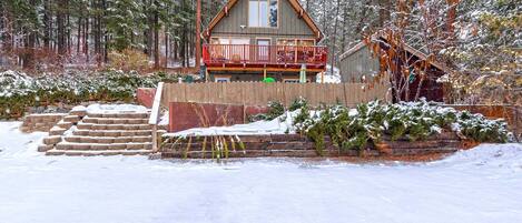 Une cabane dotée d’un balcon, entourée d’arbres couverts de neige et d’une clôture en bois.