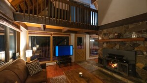 A cozy living room with a fireplace, a television, and a balcony. - Leavenworth Cabin Close To Town And Jaw Dropping View! (Leavenworth)