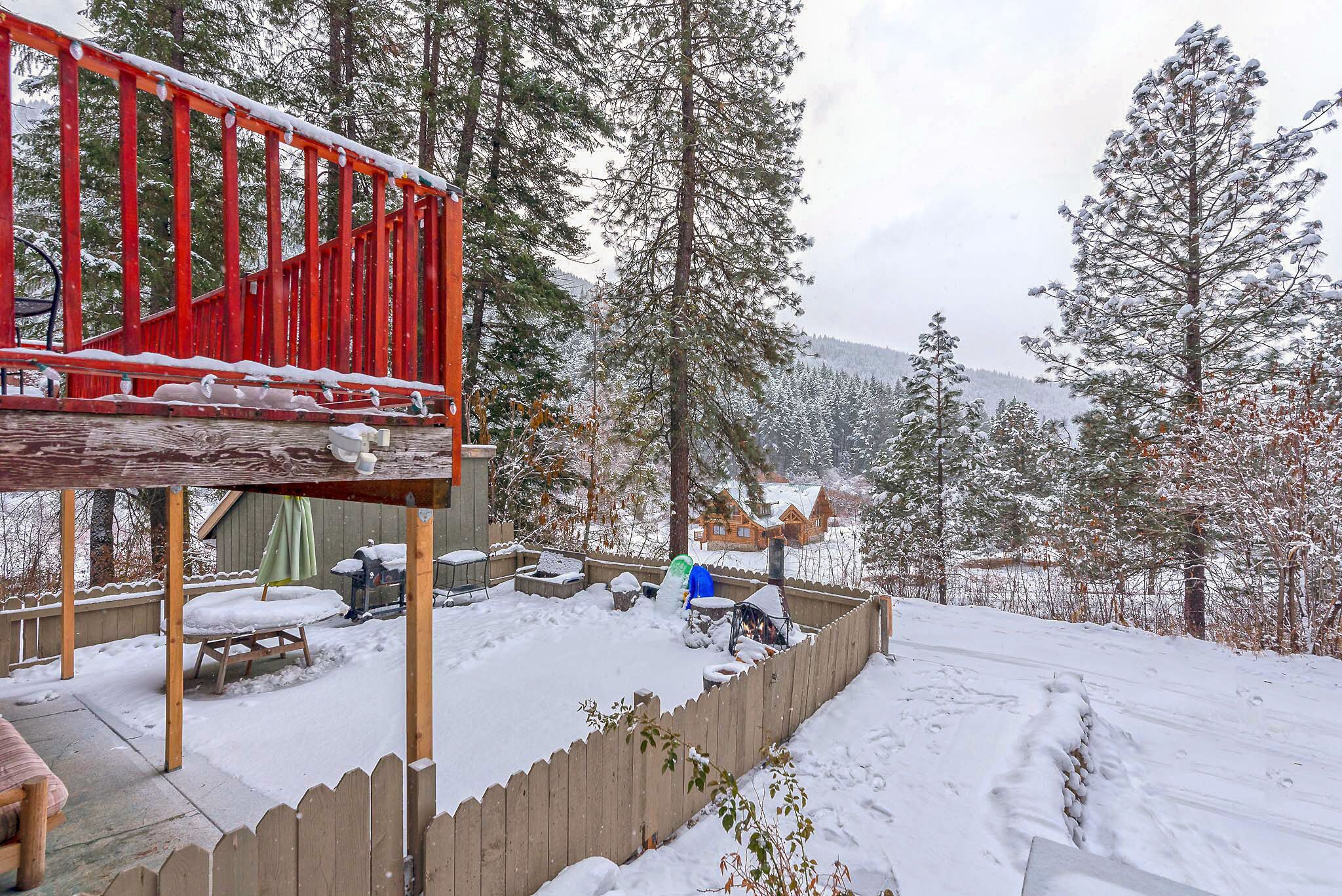 Una terraza de madera con baranda roja, rodeada de árboles cubiertos de nieve y una cerca de madera.