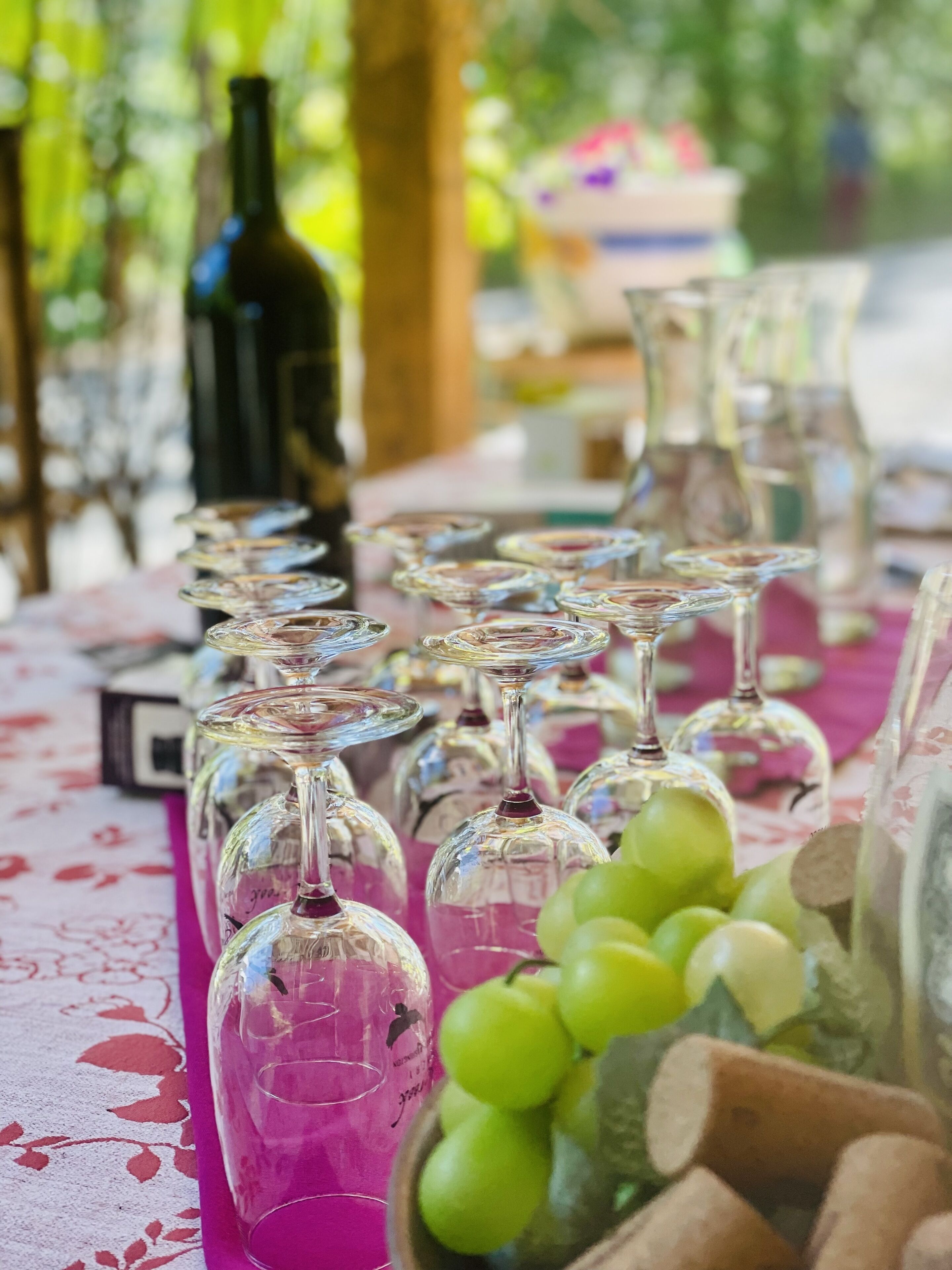 A table with multiple wine glasses and a bottle of wine, a bowl of green grapes, and a wooden container.