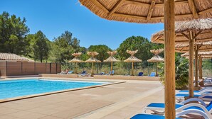 Ein Swimmingpool mit Liegestühlen und strohgedeckten Sonnenschirmen.