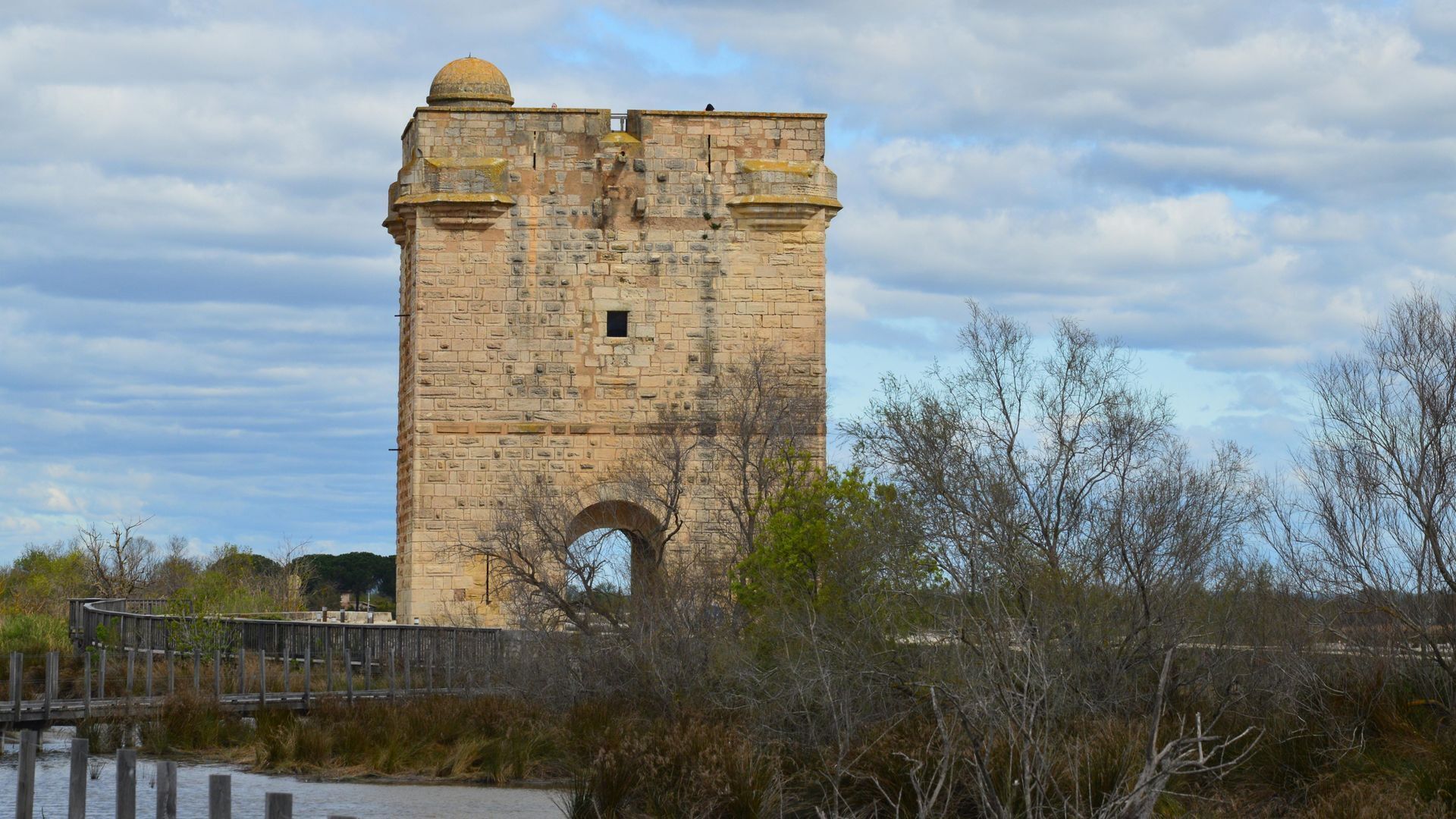 A stone tower with a dome on top, an arched entrance, and a wooden fence in the foreground.