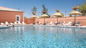 En swimmingpool med solstolar och parasoller med halmtak.