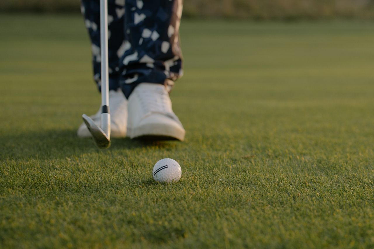A golf ball on a green with a golf club nearby.