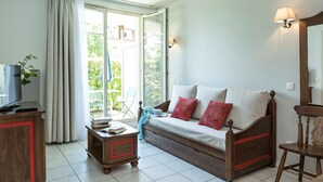 A cozy living room with a sofa, a wooden side table, a TV, and a window with curtains. - Appart Cosy le Long de la Route des Vins d'Alsace (Bergheim)