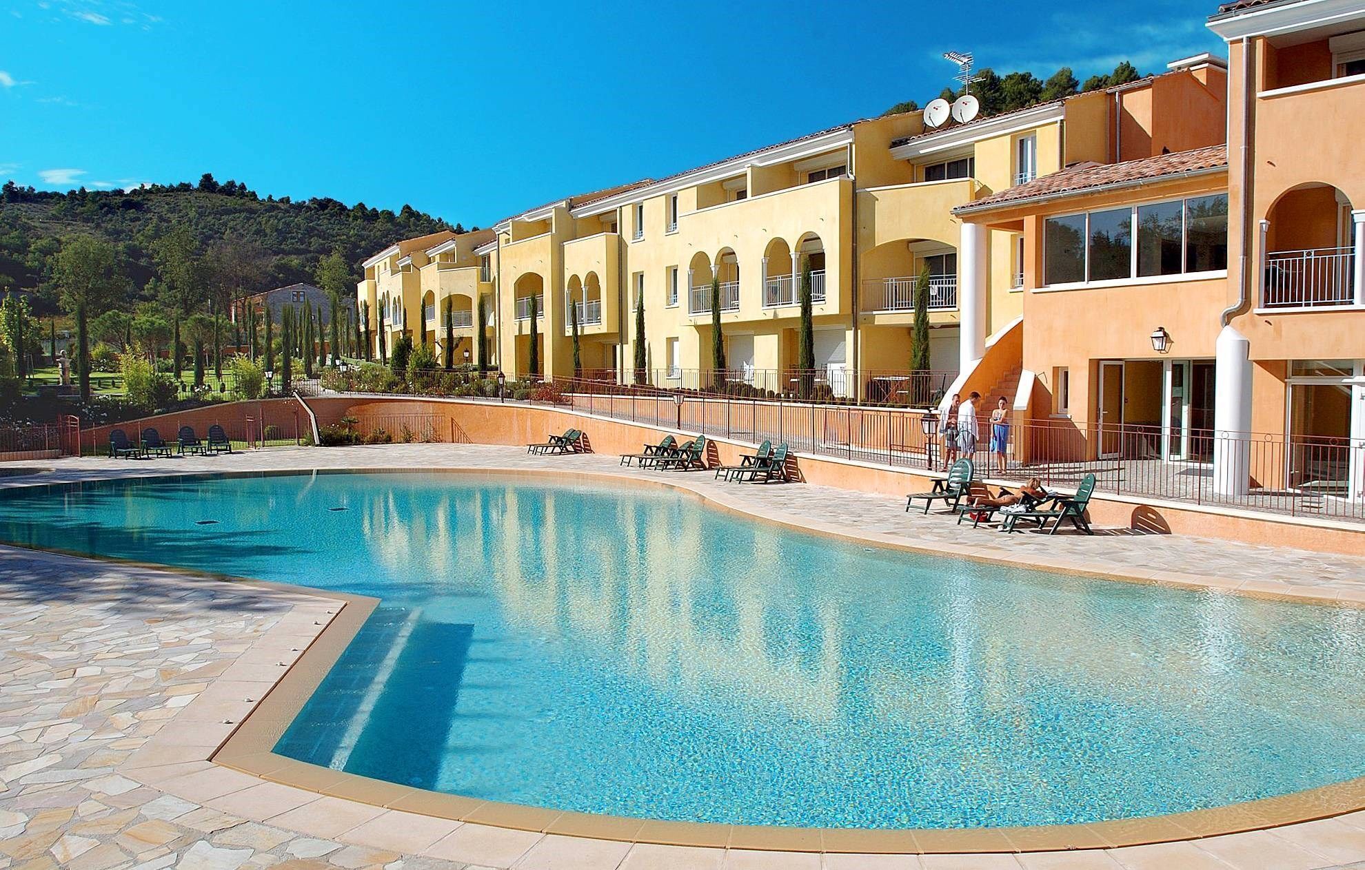 Una piscina con sillas de descanso y un edificio con balcones.