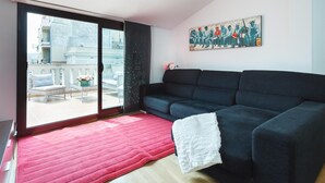 Una sala de estar moderna con un sofá oscuro, un tapete rojo y un amplio ventanal con vistas a un balcón.