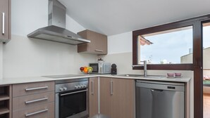 Una cocina moderna con horno integrado, microondas y lavavajillas. Hay un ventanal que proporciona luz natural y vistas al exterior.
